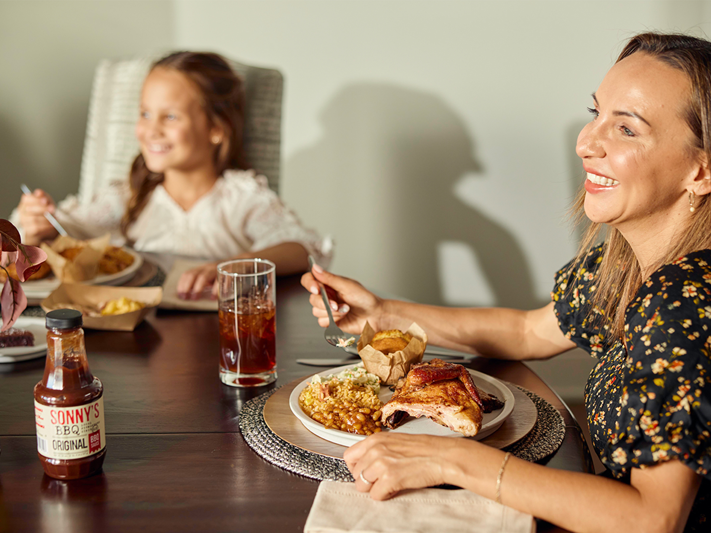 Mother and Daughter sit at table smiling with plates of BBQ