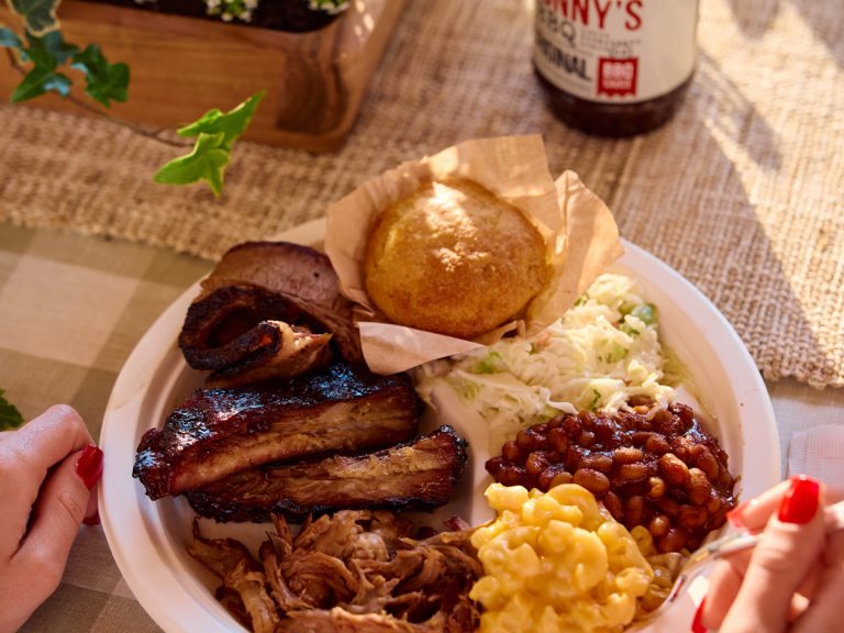 Plate full of BBQ meat and sides sits on table with bottle of Sonny's BBQ Sauce behind it