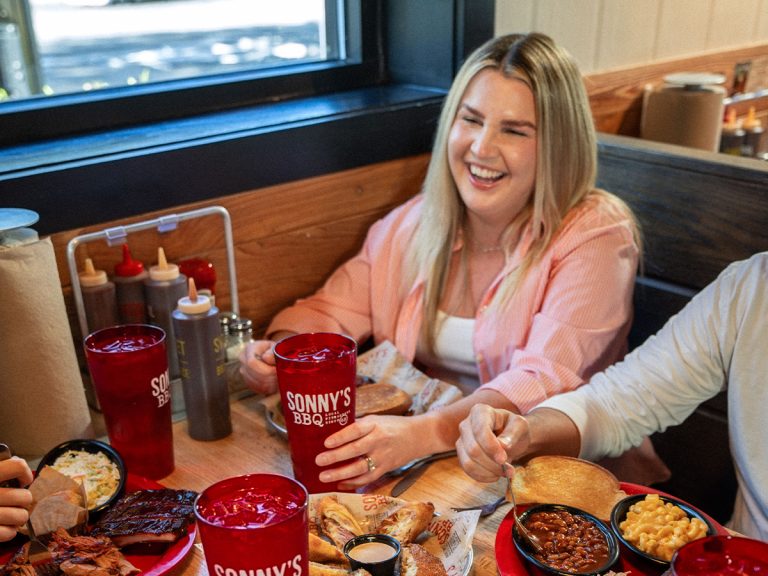 Woman smiles at Sonny's BBQ table filled with food