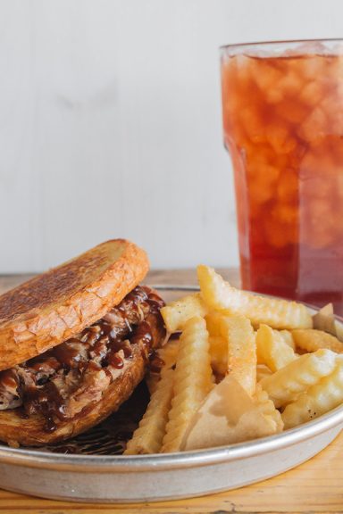 Pulled Pork Sandwich sits on plate with fries and a Sweet Tea.