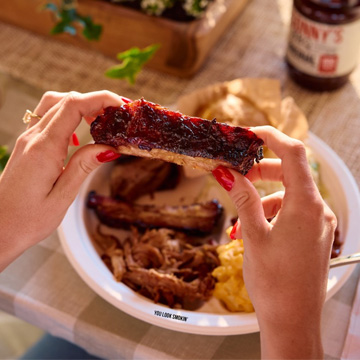 Two hands hold rib above Catering Plate on table