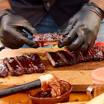 Gloved hands hold up a St. Louis Rib above a full slab laid out on a cutting board.