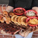 Person holding Sonny's Family Feast, a plate filled with Garlic Bread, Mac & Cheese, Coleslaw, BBQ Beans, BBQ Chicken, Sliced Pork, St. Louis Ribs, Brisket and Garlic Bread