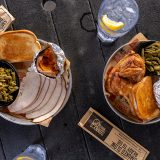 Overhead shot of black picnic table which has a Smoked Turkey Dinner and Smoked Chicken Dinner on top of it, along with silverware and two glasses full of water.