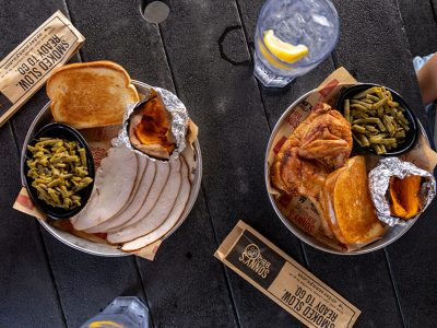 Overhead shot of black picnic table which has a Smoked Turkey Dinner and Smoked Chicken Dinner on top of it, along with silverware and two glasses full of water.