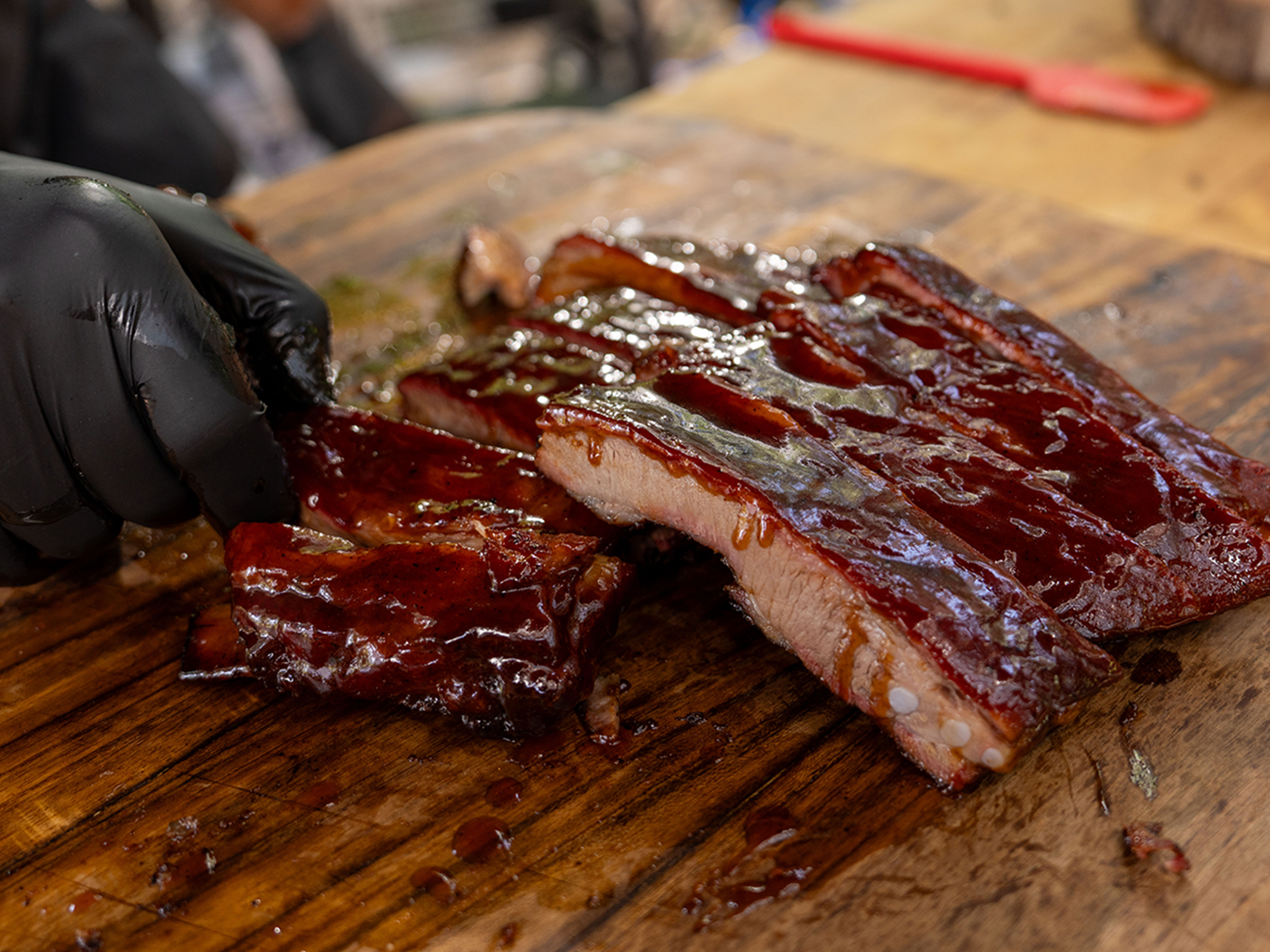 Racks of St. Louis Ribs sitting on cutting board on table with gloved hand rearranging them