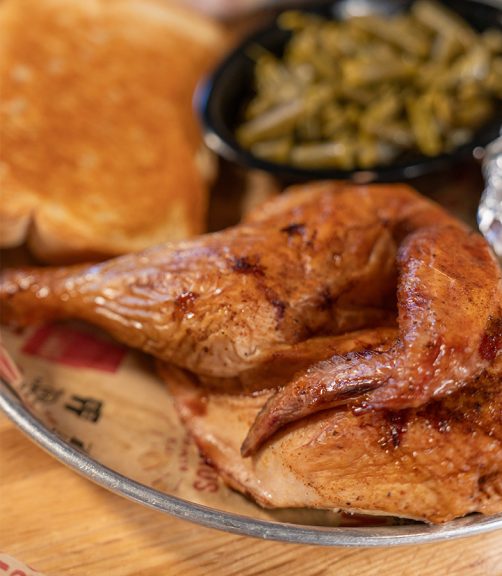 Close up of Smoked Chicken Dinner at Sonny's, with a cooked half-chicken on a plate, surrounded by green beans and garlic bread.