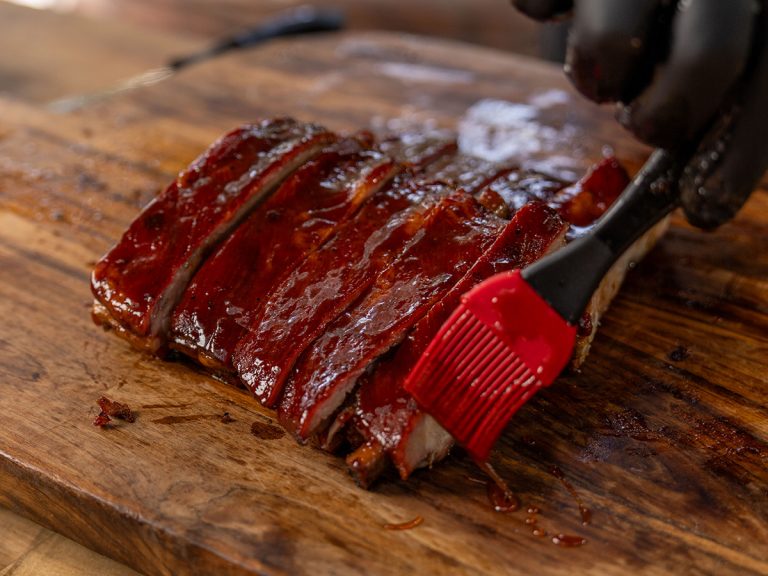 Rack of St. Louis Ribs is brushed with BBQ Sauce on Cutting Board