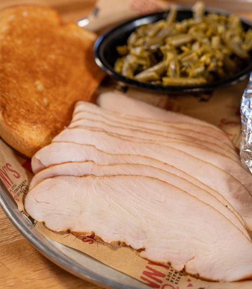 Close up of Smoked Turkey Dinner at Sonny's, with sliced turkey on a plate surrounded by green beans and garlic bread.