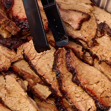 Tongs sit in tray of sliced brisket