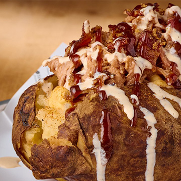 A close-up picture of Sonny's Loaded BBQ Potato, placed on a round tin with a paper liner