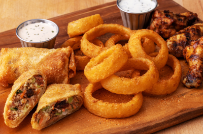 bbq pork egg rolls, onion rings and smoked wings on a cutting board