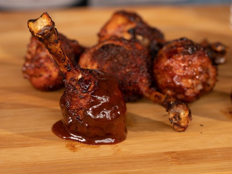 Handful of BBQ Chicken drumsticks sit on table, one of which has been dipped in Sweet BBQ Sauce.