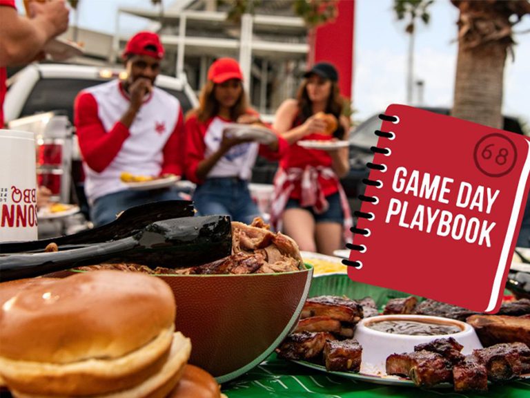 People enjoying BBQ outside football stadium, in front of them is a table lined with BBQ food and football decor. A book is superimposed on top which reads 