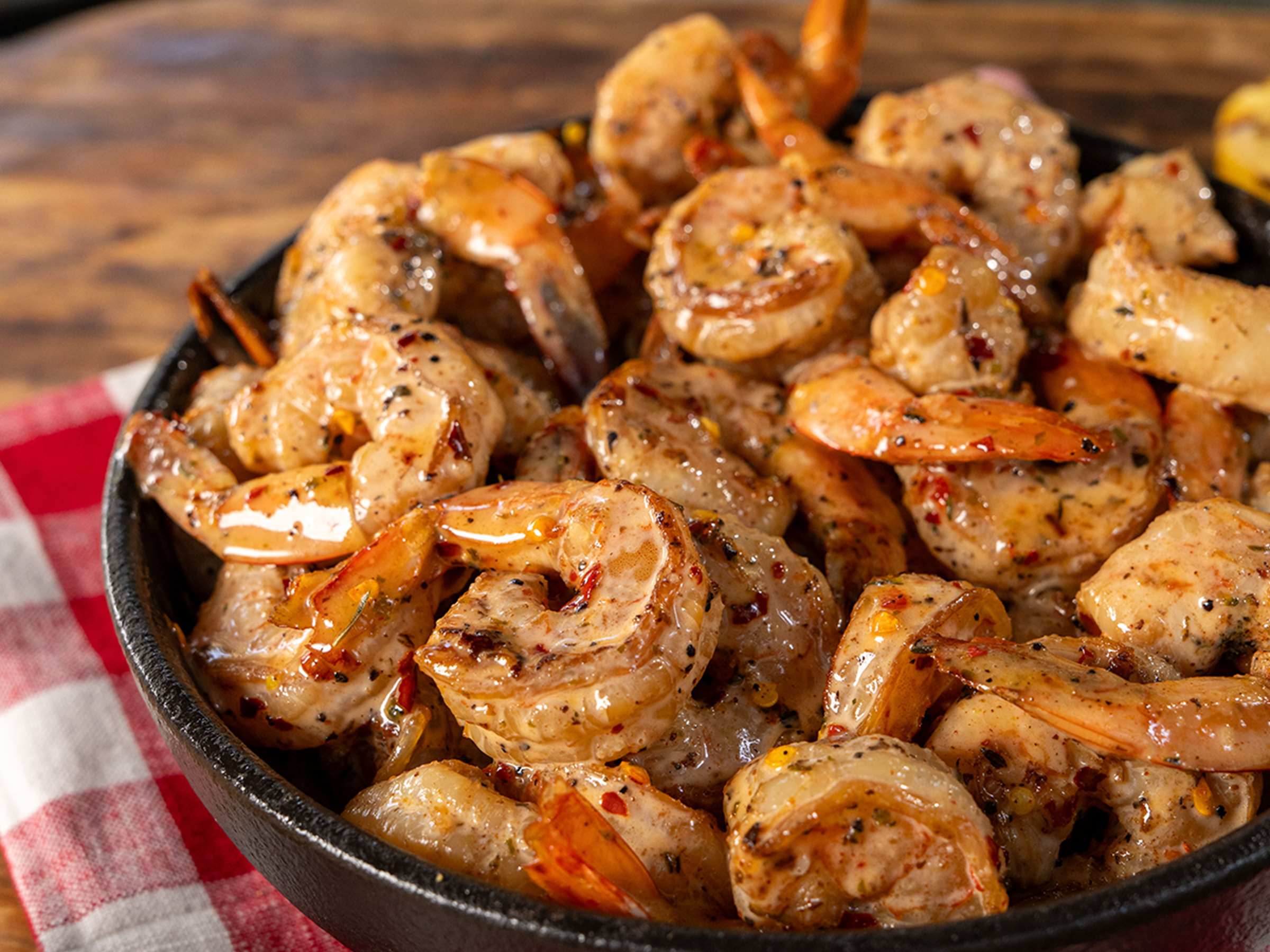 Bowl of hot honey bang bang shrimp sits on table above checkered napkin.