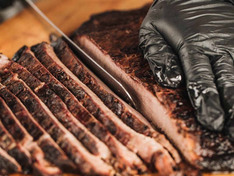 Knife slices brisket on cutting board.