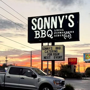 Sun rises behind Sonny's BBQ Sign in parking lot, reader board says 