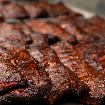 About a dozen full racks of ribs lay across each other across multiple cutting boards.