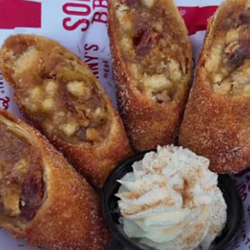 Four Pecan Pie Egg Rolls sit atop lined paper with small dish of whipped cream in the middle.