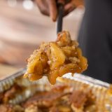 Scoop of Apple Cobbler sits on spoon above pan of cobbler.