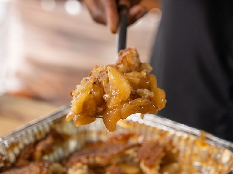 Scoop of Apple Cobbler sits on spoon above pan of cobbler.