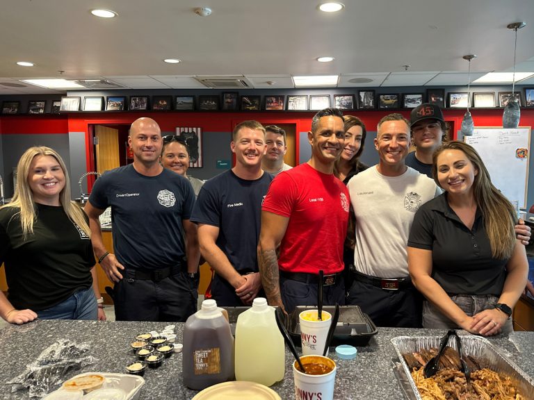 Group of Clearwater firefighters stands with Sonny's team members in front of BBQ spread.