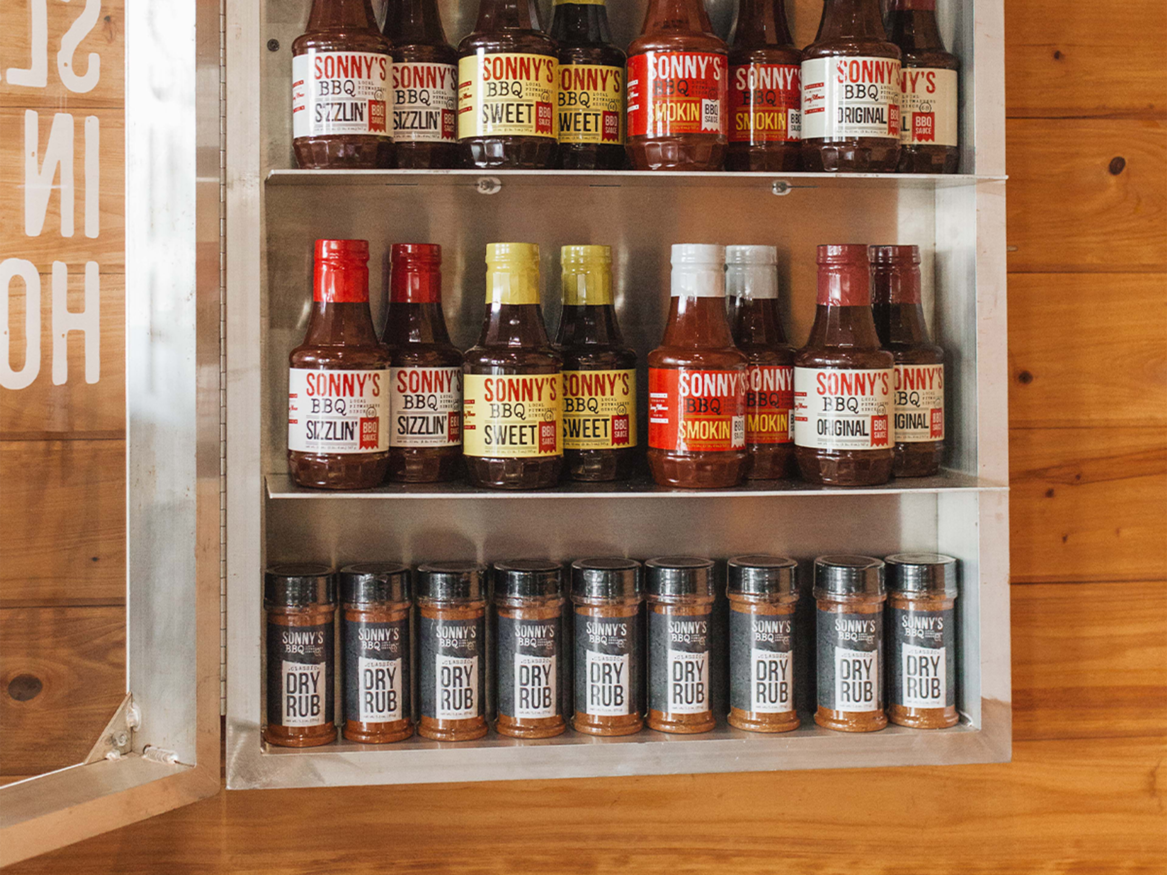 Open cabinet displays bottles of Sonny's BBQ Sauce and Rubs