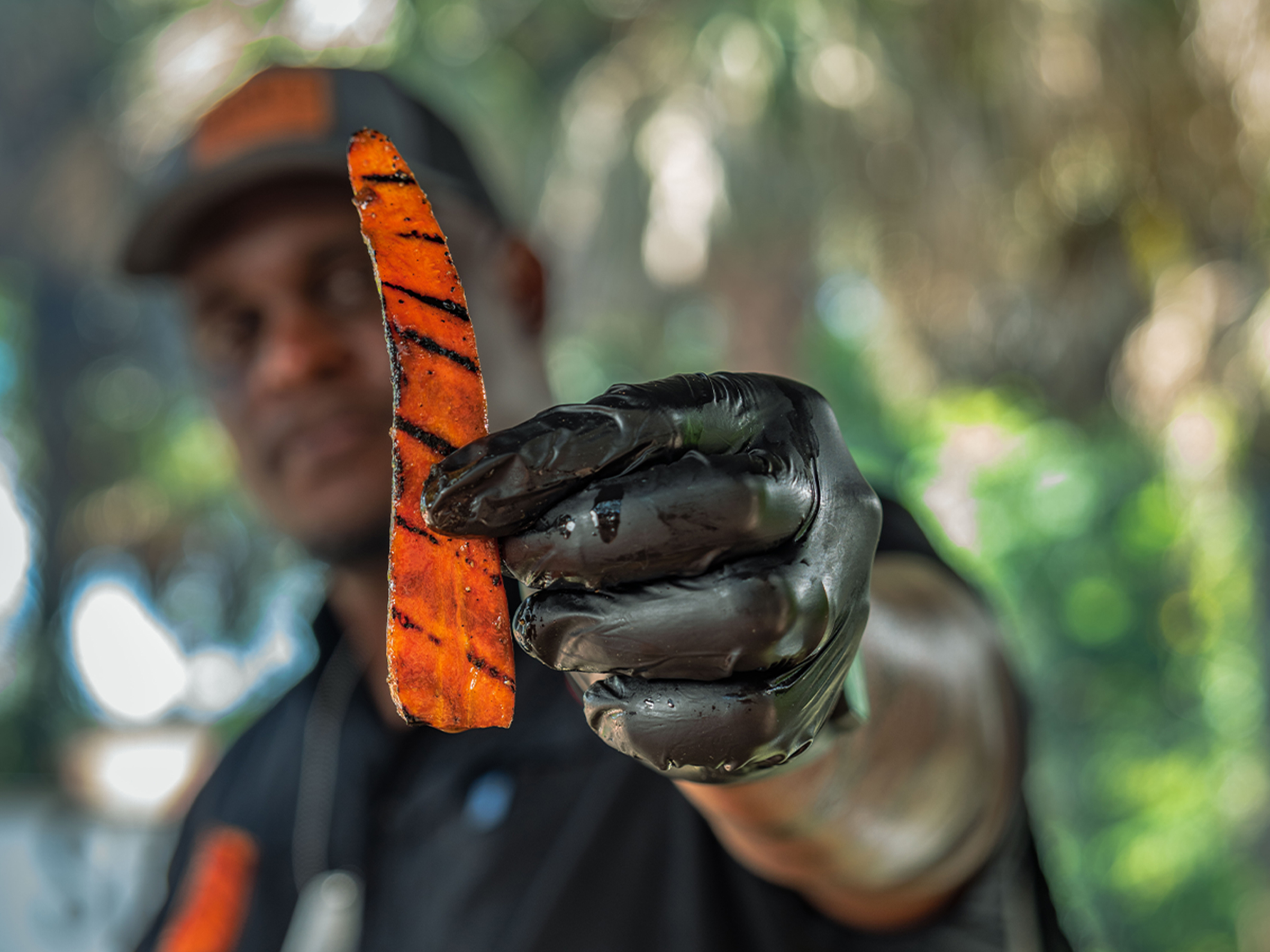Pitmaster holds grilled carrot slice up to camera.