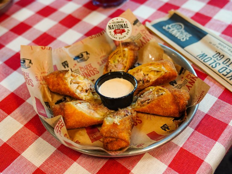 Lined tin filled with Pulled Pork Egg Rolls sits on table. Flag sticks out of one saying "I celebrated National Pulled Pork Day."