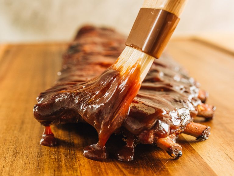 Brush bastes rack of BBQ Ribs with sauce
