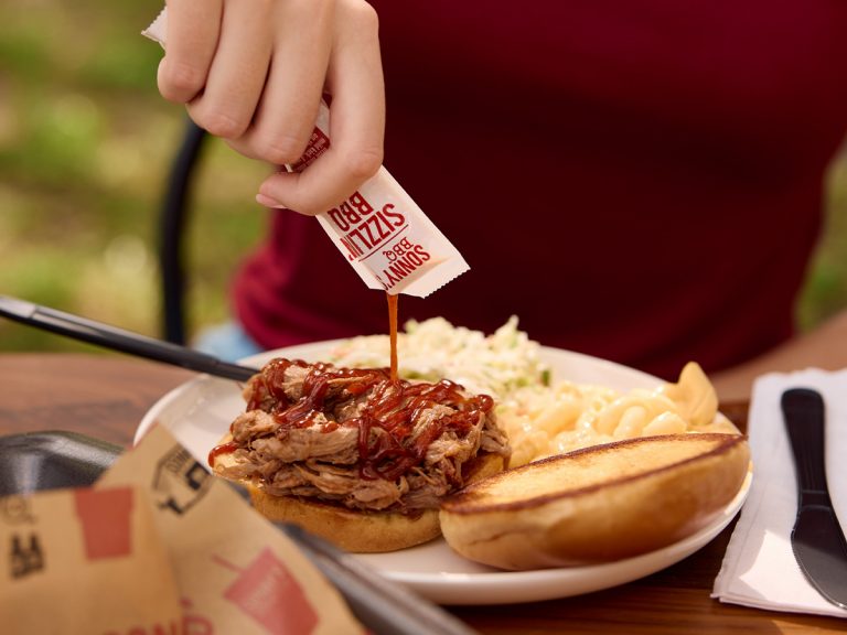 Woman squeezes Sizzlin' BBQ Sauce onto Pulled Pork Sandwich