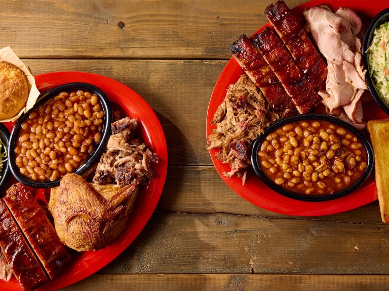 Two plates on Sonny's Originals, the Pork 3 Ways and Sonny' Sampler sit next to each other on wood surface