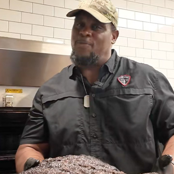 Pitmaster holds brisket in front of smoker.