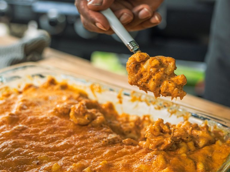 Man holding spoon scoops out spoonful of Smoked Macaroni and Cheese from dish.