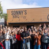 Man smiles and crowd cheers behind him moments after ribbon-cutting at Sonny's BBQ in Wesley Chapel