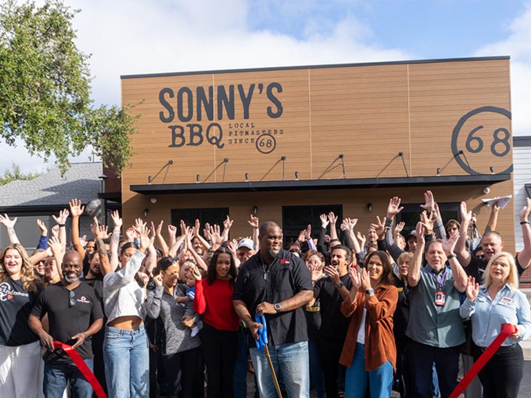 Man smiles and crowd cheers behind him moments after ribbon-cutting at Sonny's BBQ in Wesley Chapel