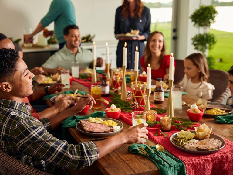 Family and friends sit around decorated holiday dinner table, filled with Sonny's Catering options.