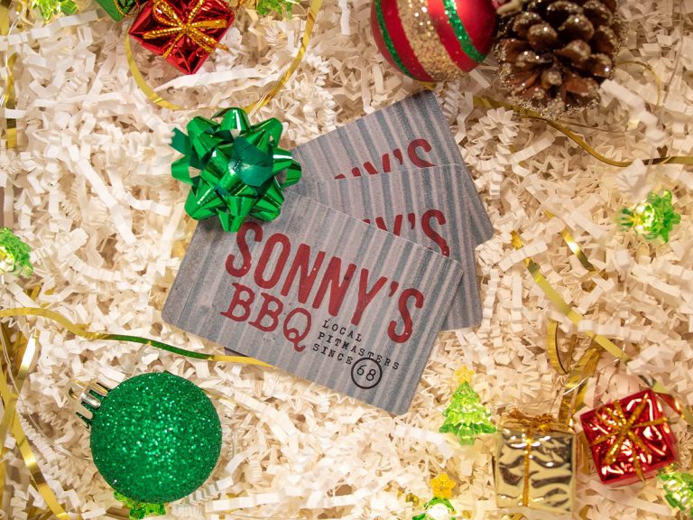 Stack of 3 Sonny's Gift Cards on top of decorative paper fill and surrounded by holiday decor.