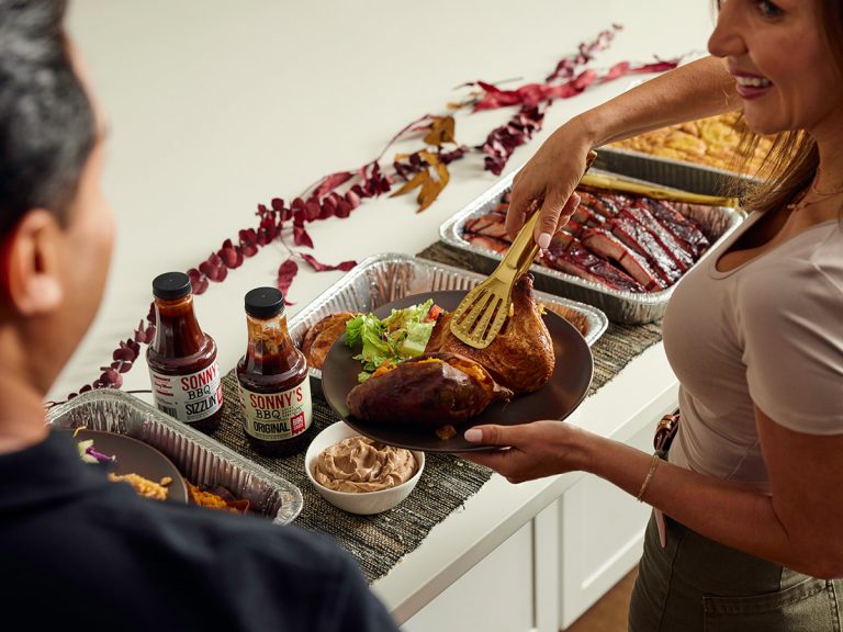 Woman picks up chicken and places it on plate filled with Sonny's Catering sides.