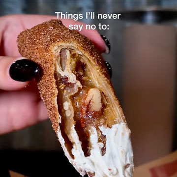 Hand holds pecan pie egg roll dipped in whipped cream