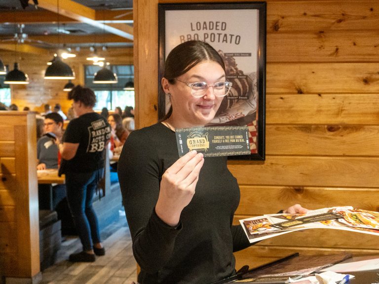 Hostess holds up Free Pork Big Deal Coupon and smiles during Wesley Chapel Grand Reopening