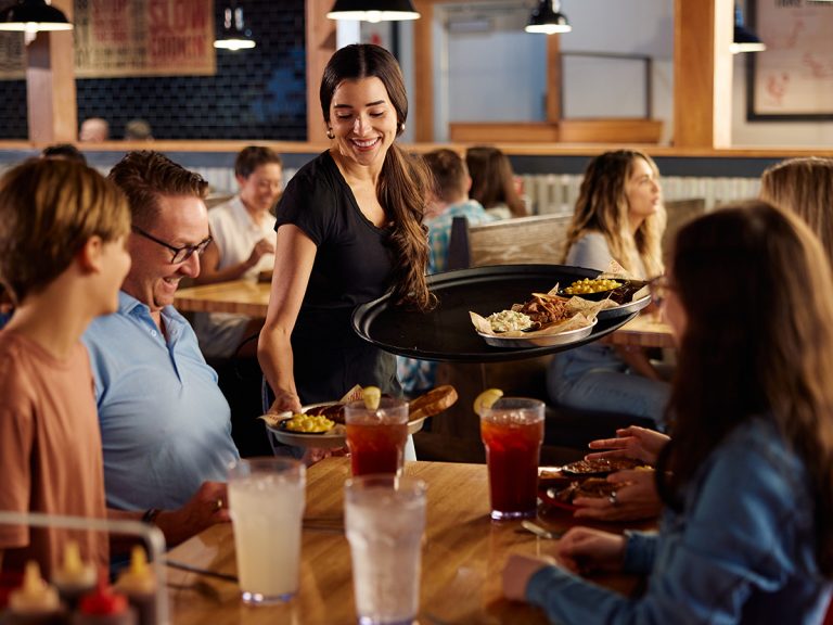 Server hands plate of BBQ to full table.