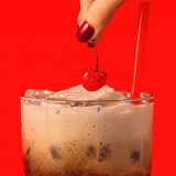 A hand places a cherry on Sonny's Root Beer Cream Soda.