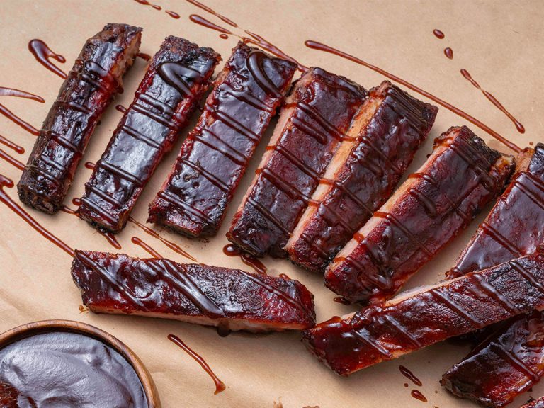 Array of St. Louis Ribs, one of the rib types, sits on butcher paper decorated with a drizzle of BBQ Sauce.