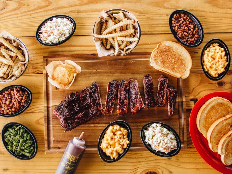Slab of ribs sits on cutting board surrounded by bowls filled with Sonny's sides.