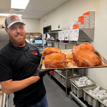 Pitmaster holds up tray of seasoned Pork Butts