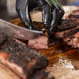 Knife slicing smoked beef ribs on cutting board.