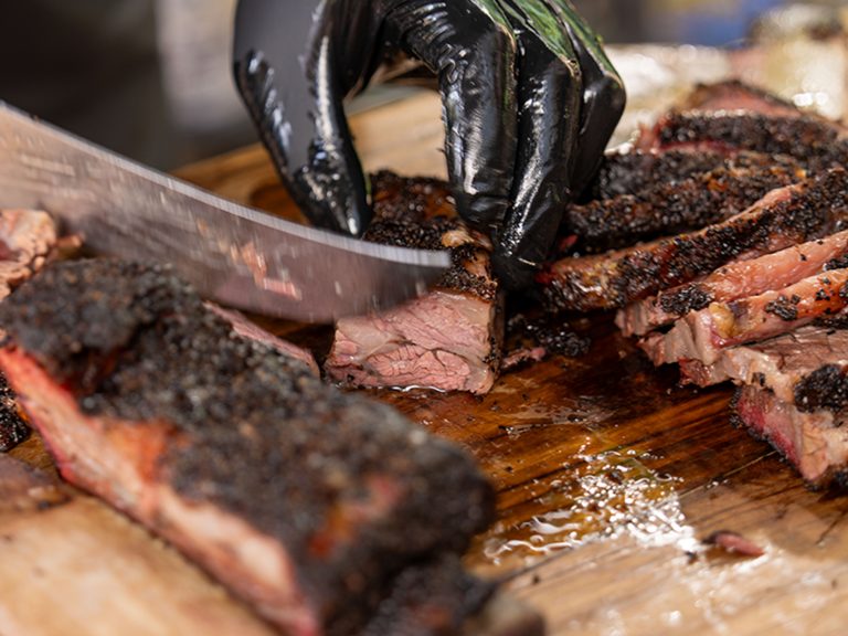 Knife slicing smoked beef ribs on cutting board.