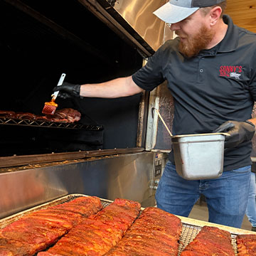 Pitmaster slathers BBQ Sauce on rack of ribs in smoker.