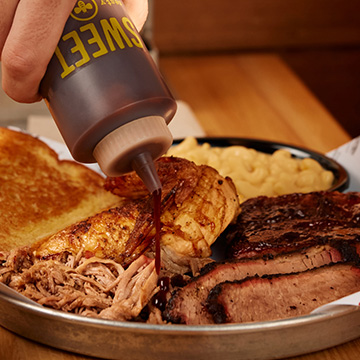 Person squeezes sauce onto BBQ plate full of food